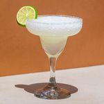 Frozen Margarita in curved margarita glass with salt rim and lime wheel, on orange background