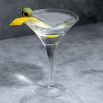 Vodka Martini in a classic V-shaped Martini class with both lemon twist and olive garnish, on dark marble background